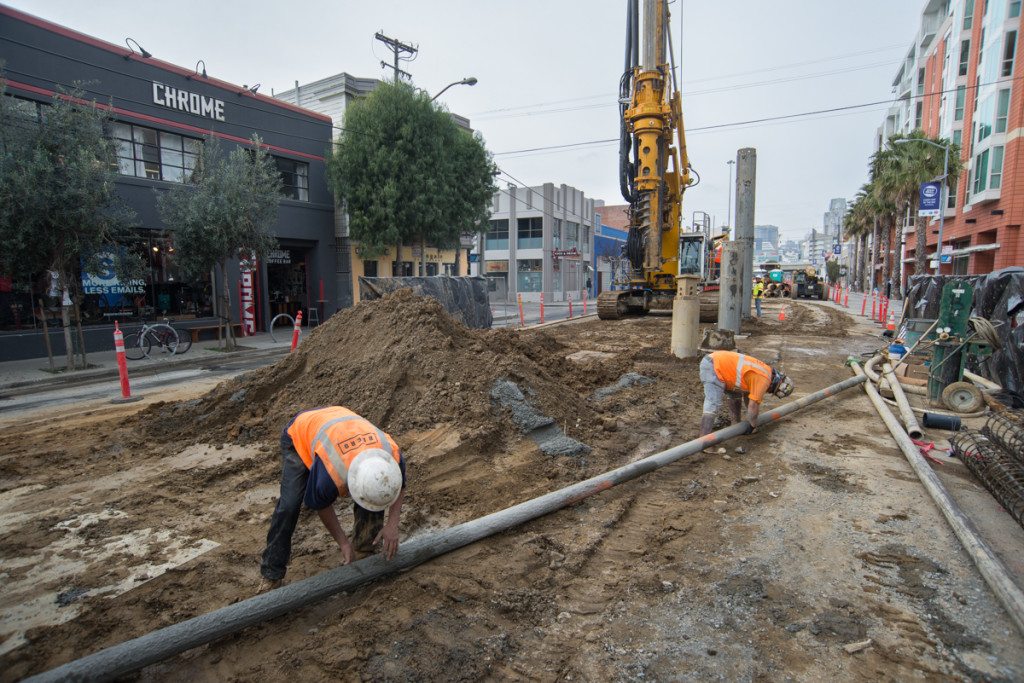 Workers lift a section of pipe that will be used to pour concrete into the excavated pile shafts. The concrete piles form the foundation of the future 4th and Brannan Station.